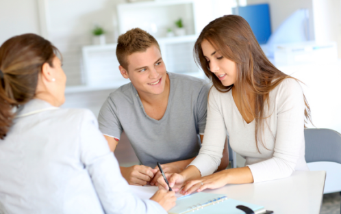 Junges Paar im Gespräch mit einer Beraterin am Schreibtisch – Anmeldung oder Beratungssituation.